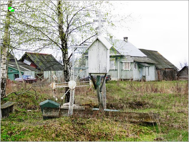 Окшово. Церковь Рождества Христова. фасады, Вид с востока. Часовня в виде деревянного домика на стволе спиленного дерева. Рядом в землю врыт кованый крест от Рождественской церкви