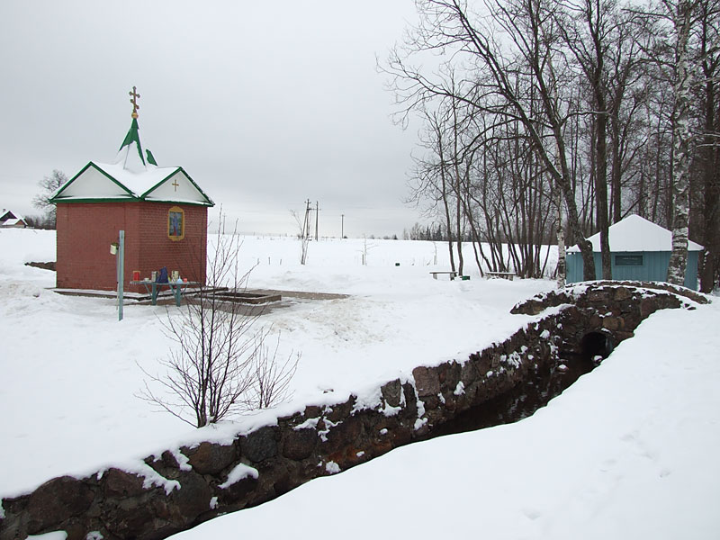Часовня Успения Пресвятой Богородицы над источником, Куремяэ (Ида-Вирумаа, Эстония). общий вид в ландшафте, В правой части кадра за мостиком – купальня