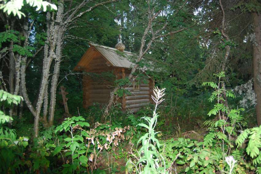 Часовня Тихвинской иконы Божией Матери, Шишкина (Плесецкий район, Архангельская область). общий вид в ландшафте, Вид с северо-востока на часовню и памятный крест на месте сгоревшей старой часовни.